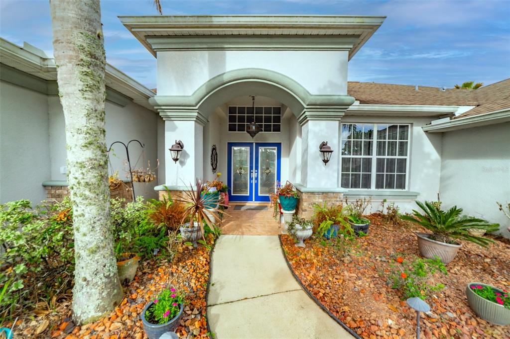 The exterior of a house features a covered entryway with blue double doors and landscaping — 4347 GEVALIA DRIVE, BROOKSVILLE, FL