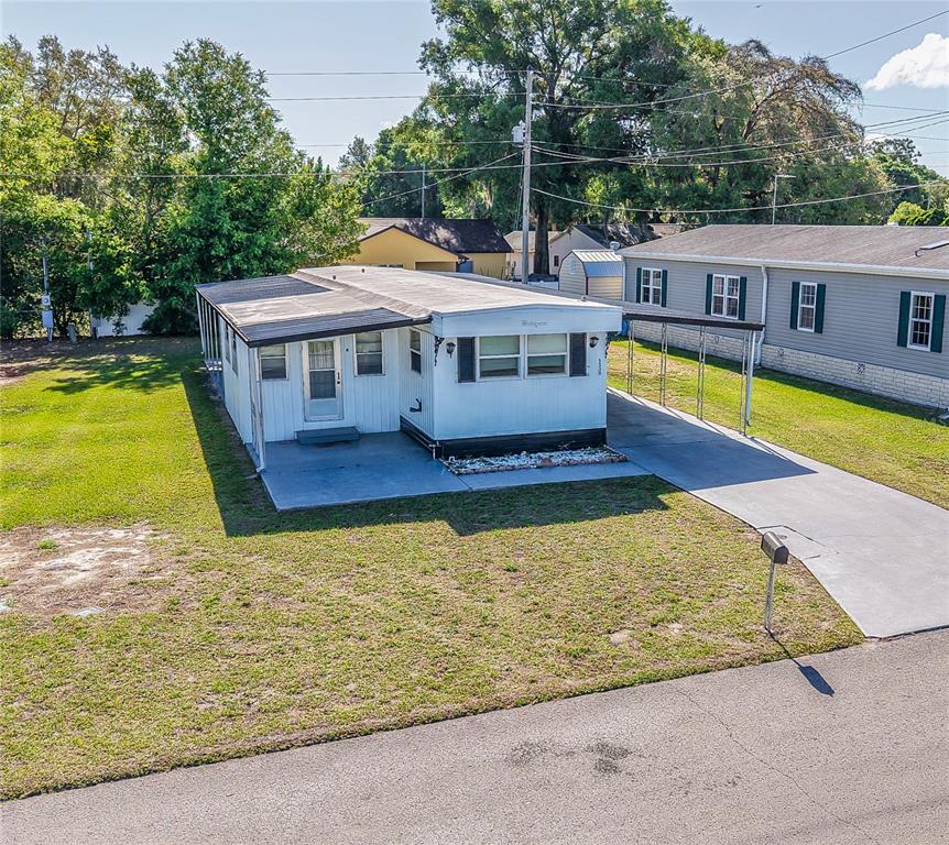 An elevated exterior view of a single-story mobile home with a concrete driveway and carport — 5330 BETMAR DRIVE, ZEPHYRHILLS, FL