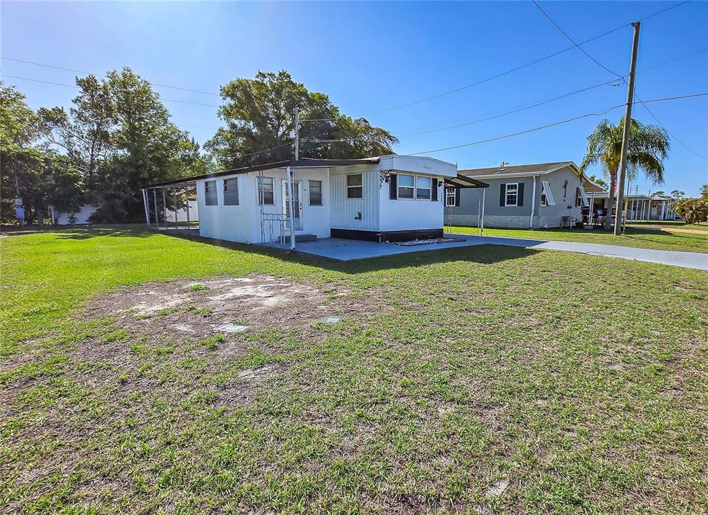 A white mobile home with a metal carport sits on a grassy lot — 5330 BETMAR DRIVE, ZEPHYRHILLS, FL