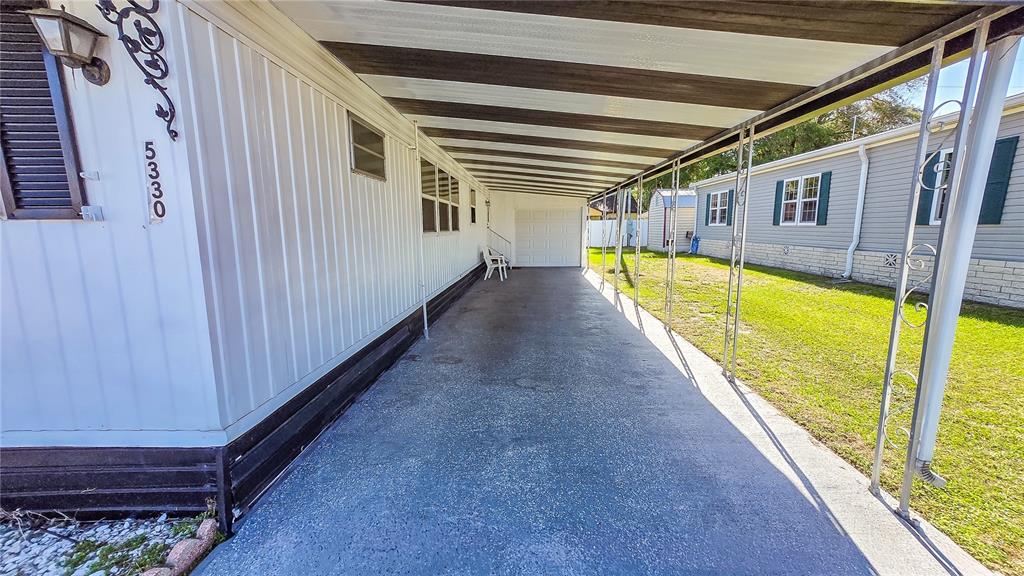 A long, covered concrete carport runs alongside a mobile home with white vertical siding — 5330 BETMAR DRIVE, ZEPHYRHILLS, FL