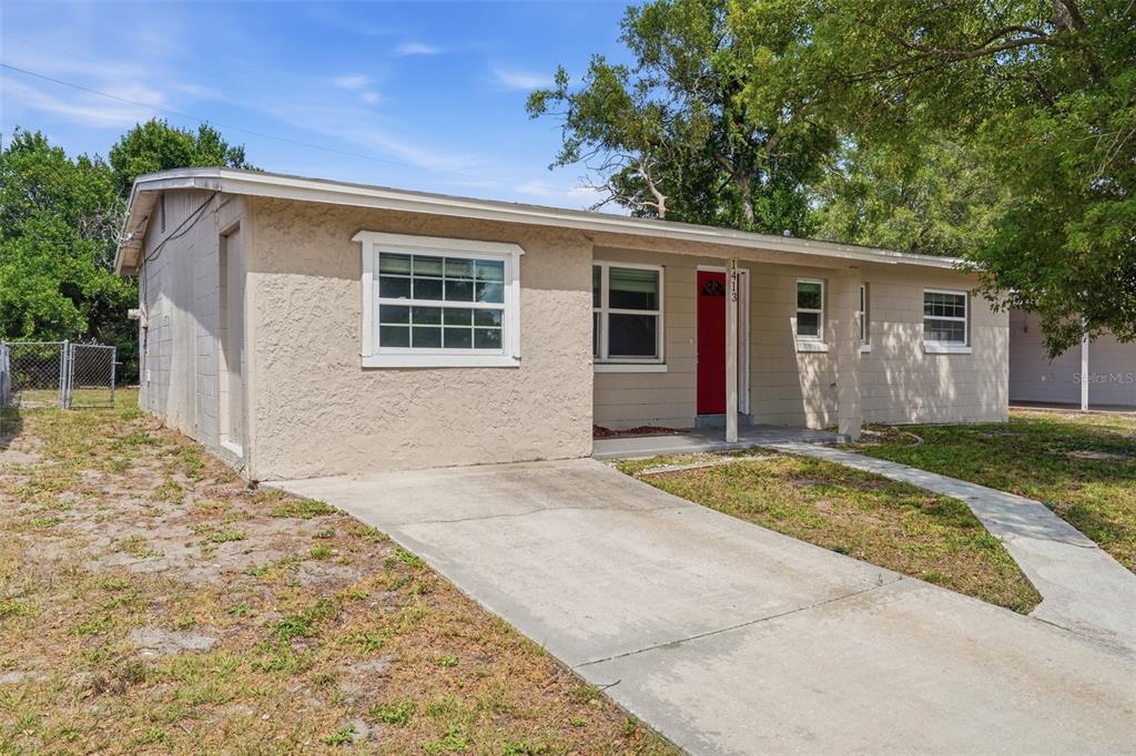 A single-story house with a beige stucco exterior, a concrete driveway, and a red front door — 1413 SUNRIDGE ROAD, ORLANDO, FL