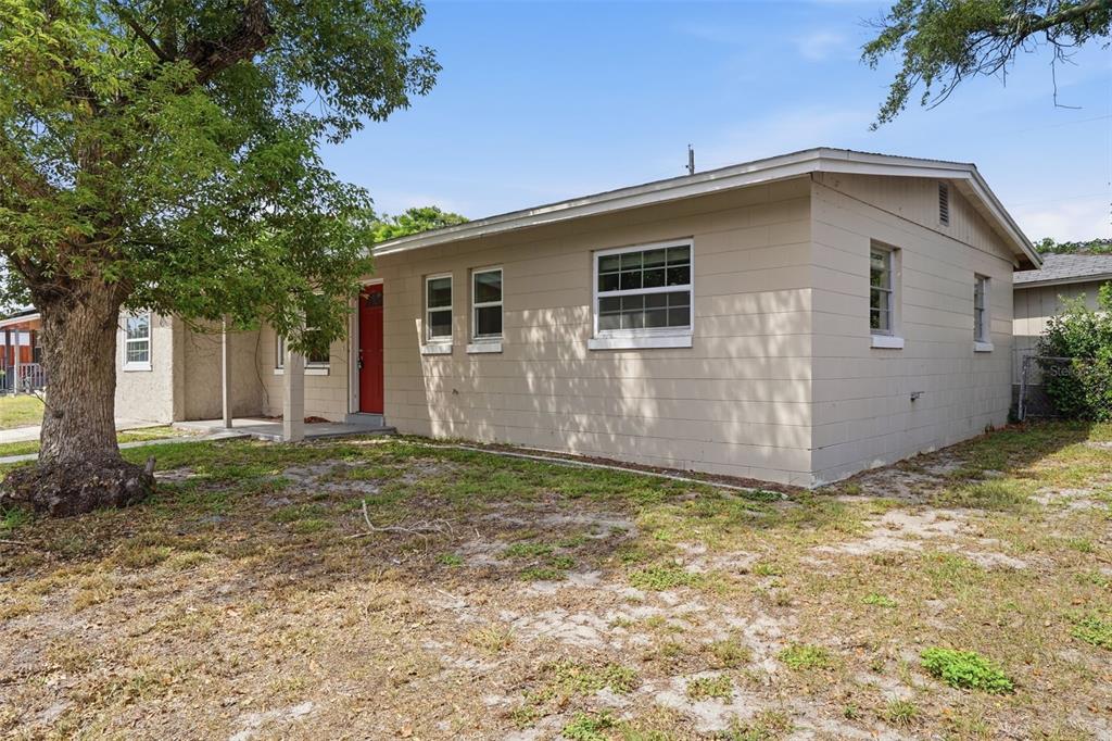 A single-story house with tan concrete block walls, a red front door, and a tree — 1413 SUNRIDGE ROAD, ORLANDO, FL