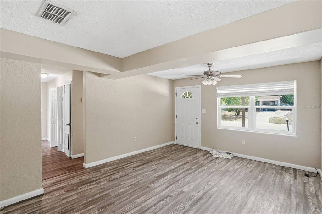 A living room with light-colored walls, wood-look flooring, a ceiling fan, and an entry door — 1413 SUNRIDGE ROAD, ORLANDO, FL