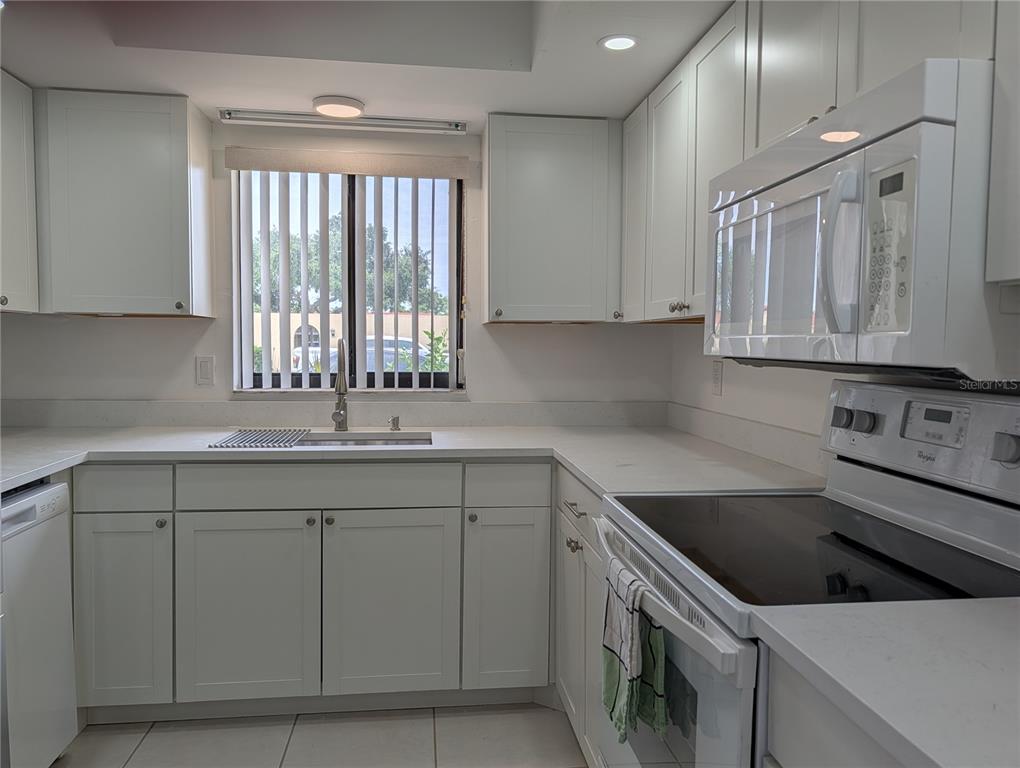 A kitchen with white cabinets, white countertops, and white appliances under a window — 5716 12TH AVENUE W UNIT 5716, BRADENTON, FL
