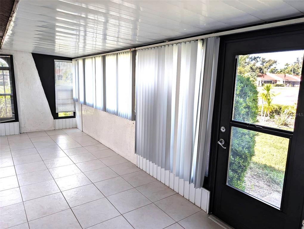 A sunroom features white tiled flooring, vertical blinds, and a black glass-paneled exterior door — 5716 12TH AVENUE W UNIT 5716, BRADENTON, FL