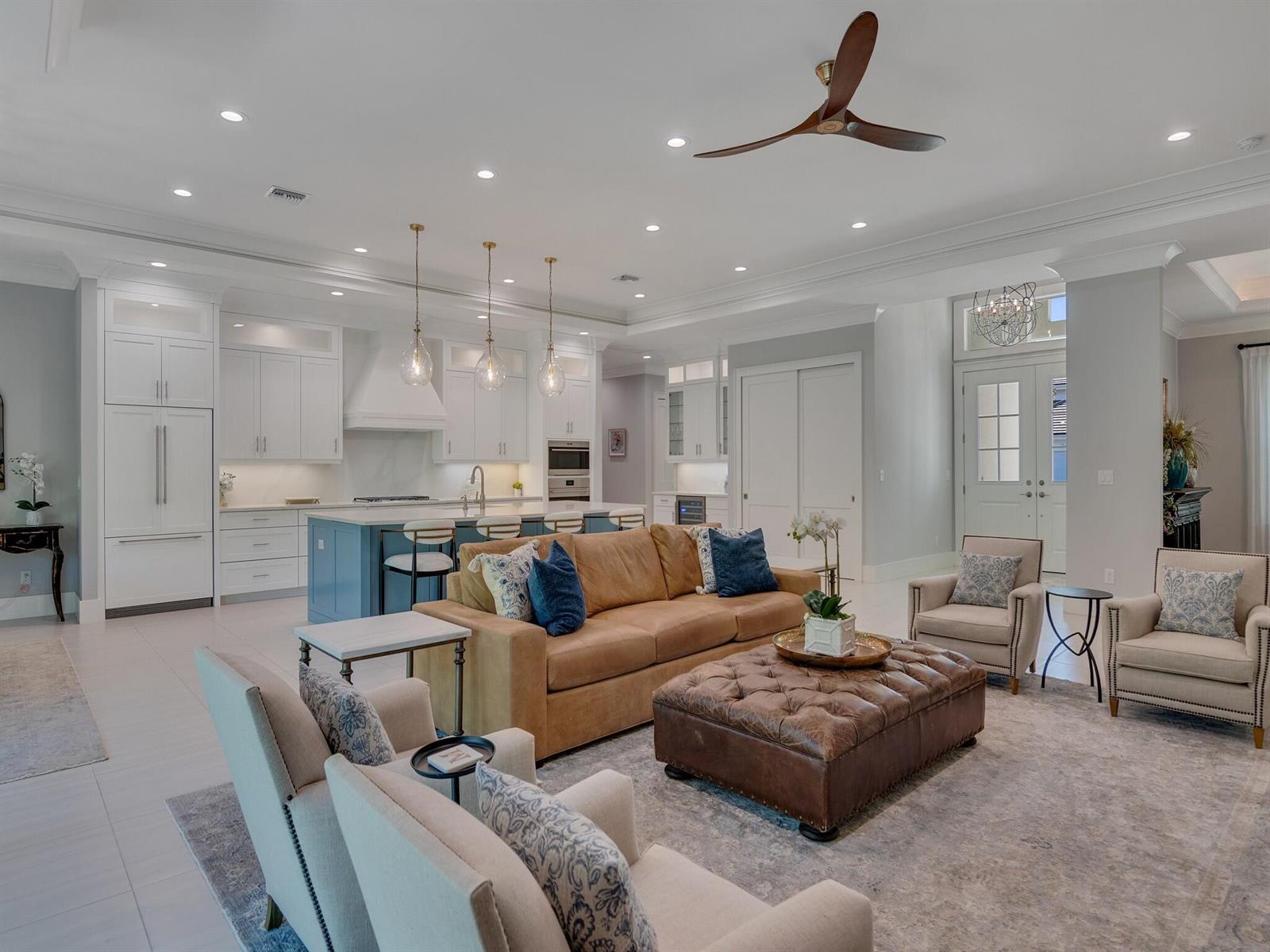 An open-concept living room and kitchen featuring a tan sofa, leather ottoman, and white cabinetry — VERO BEACH, FL
