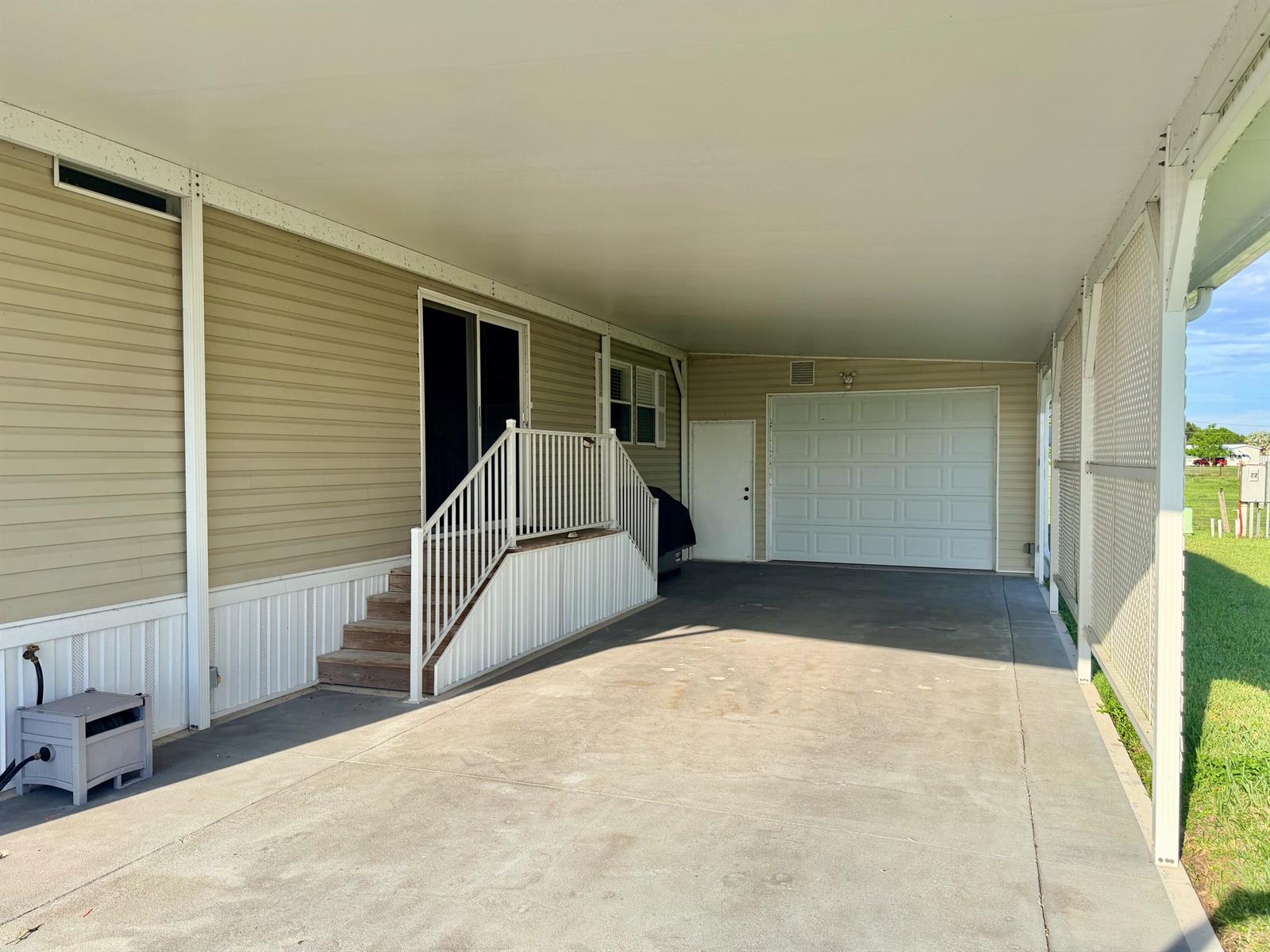 A covered concrete carport features a white garage door, a side door, and stairs — 1601 SE Us Highway 441 # 22, Okeechobee FL 34974, OKEECHOBEE, FL
