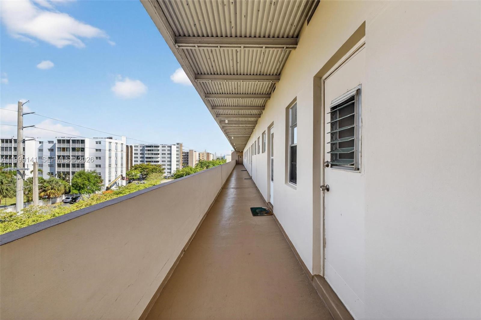 An outdoor apartment building walkway features a covered corridor with white walls and doors — 300 NE 14th Ave # 505, Hallandale Beach FL 33009, HALLANDALE BEACH, FL