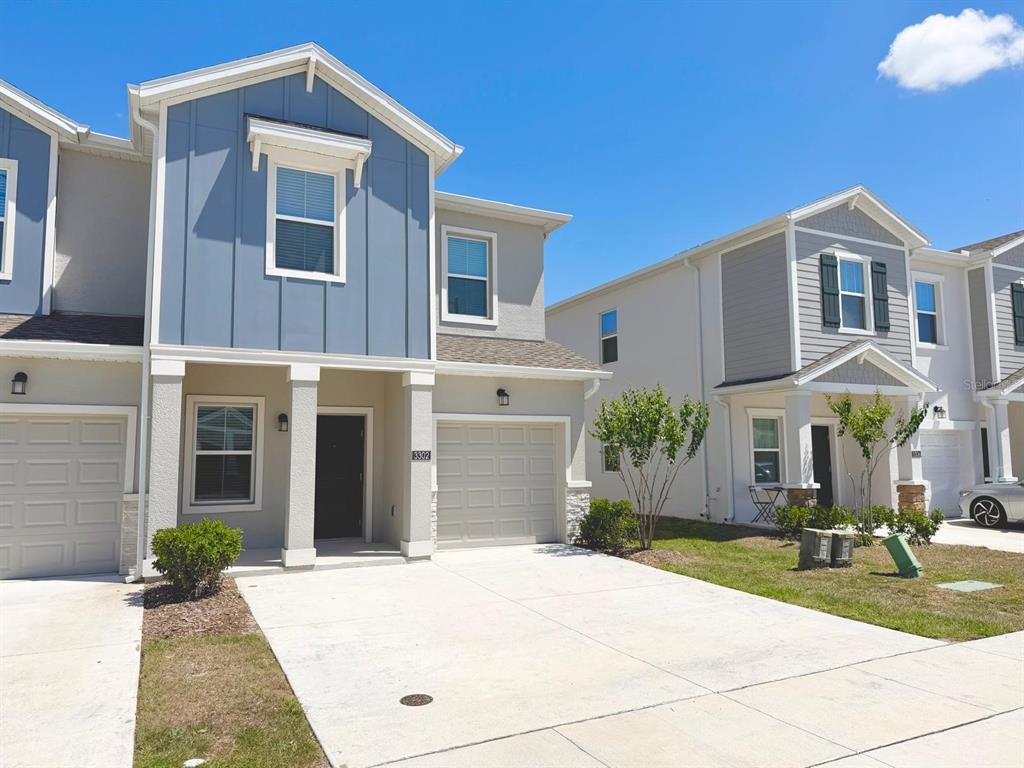 A two-story townhouse with a blue vertical-siding gable, beige stucco, and a concrete driveway — 3302 LAURENT LOOP, DAVENPORT, FL