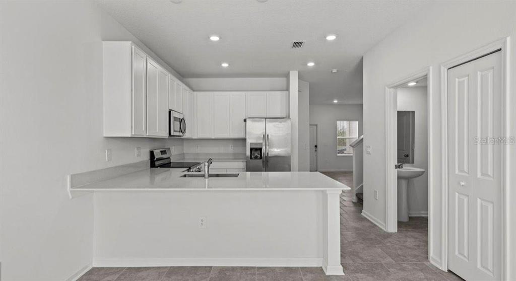 A kitchen with white cabinets, stainless steel appliances, and a quartz countertop breakfast bar — 3302 LAURENT LOOP, DAVENPORT, FL