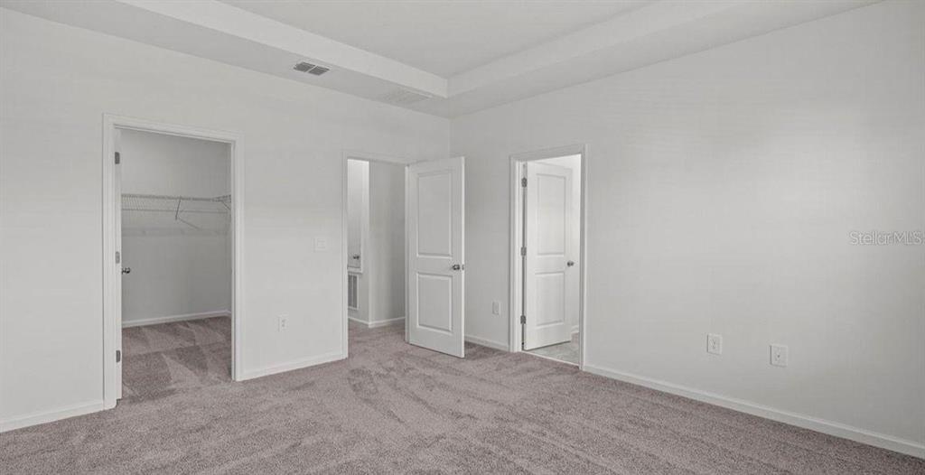 An empty bedroom with gray carpet, white walls, and three open doorways — 3302 LAURENT LOOP, DAVENPORT, FL