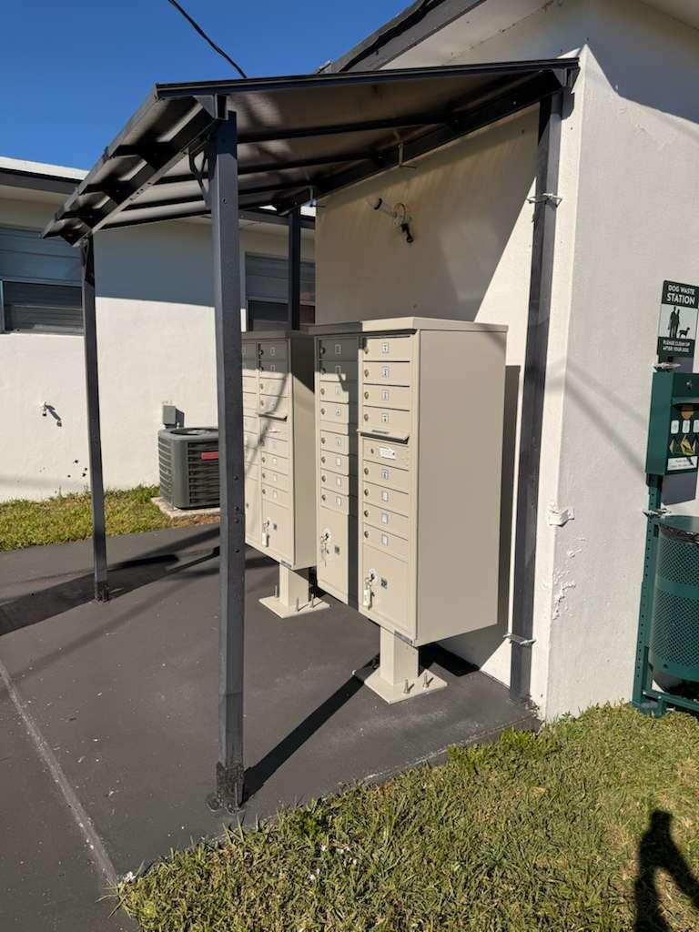 Two beige metal mailbox clusters stand under a covered outdoor structure next to a building — 1885 40th Avenue Unit 4, Vero Beach FL 32960, VERO BEACH, FL