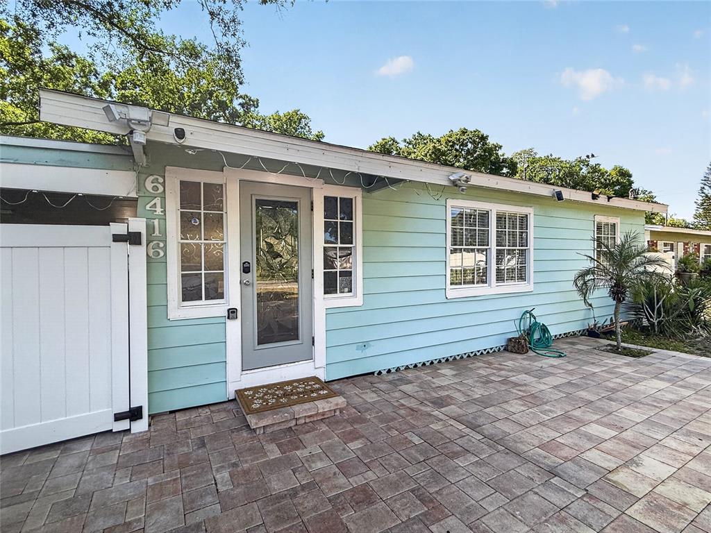 A light blue house exterior features a paved patio, a glass-paneled door, and white trim — 6416 N ORLEANS AVENUE, TAMPA, FL