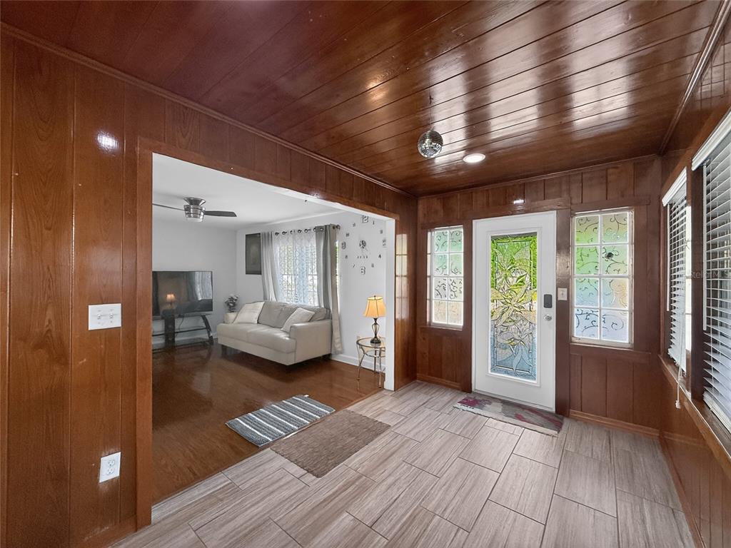 A sunroom with wood-paneled walls and ceilings leads into a living room with white walls — 6416 N ORLEANS AVENUE, TAMPA, FL