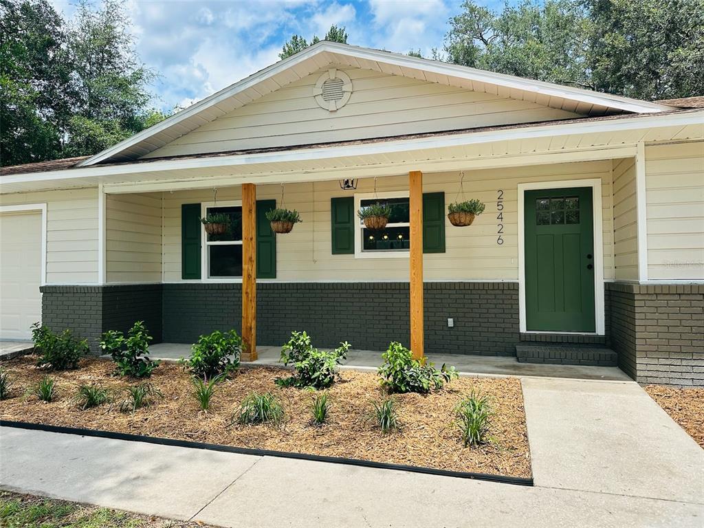 A single-story house exterior features cream siding, dark green shutters and door, and brick accents — 25426 SW 18TH AVENUE, NEWBERRY, FL