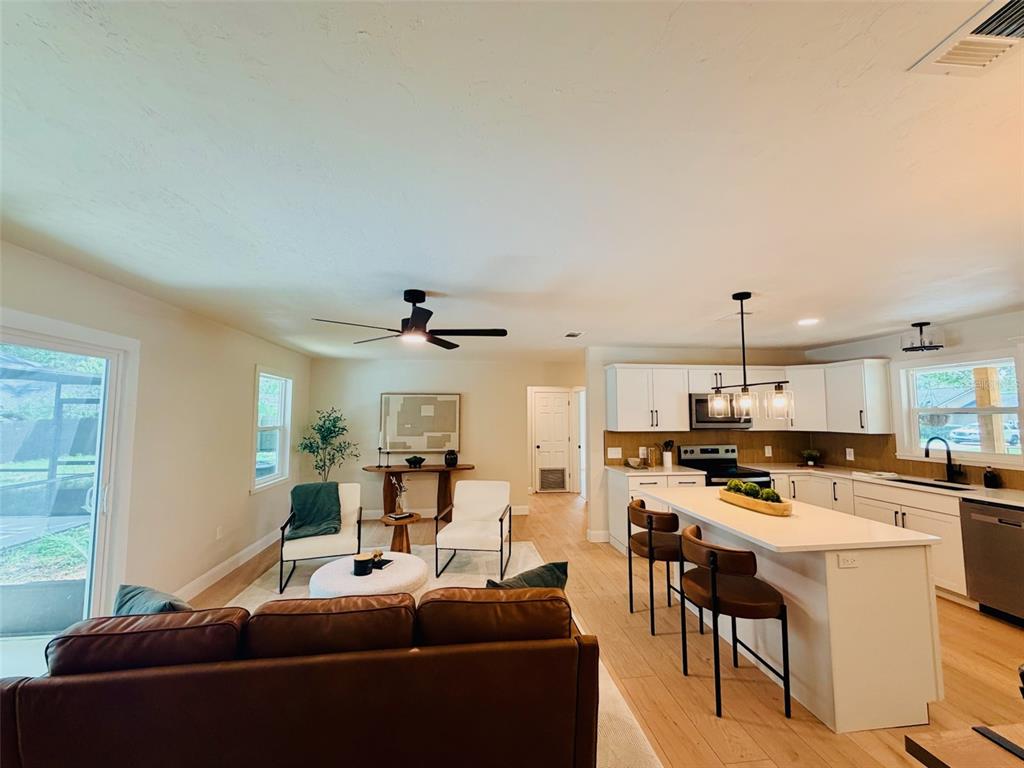 An open-concept living room and kitchen featuring white cabinetry, a kitchen island, and leather seating — 25426 SW 18TH AVENUE, NEWBERRY, FL