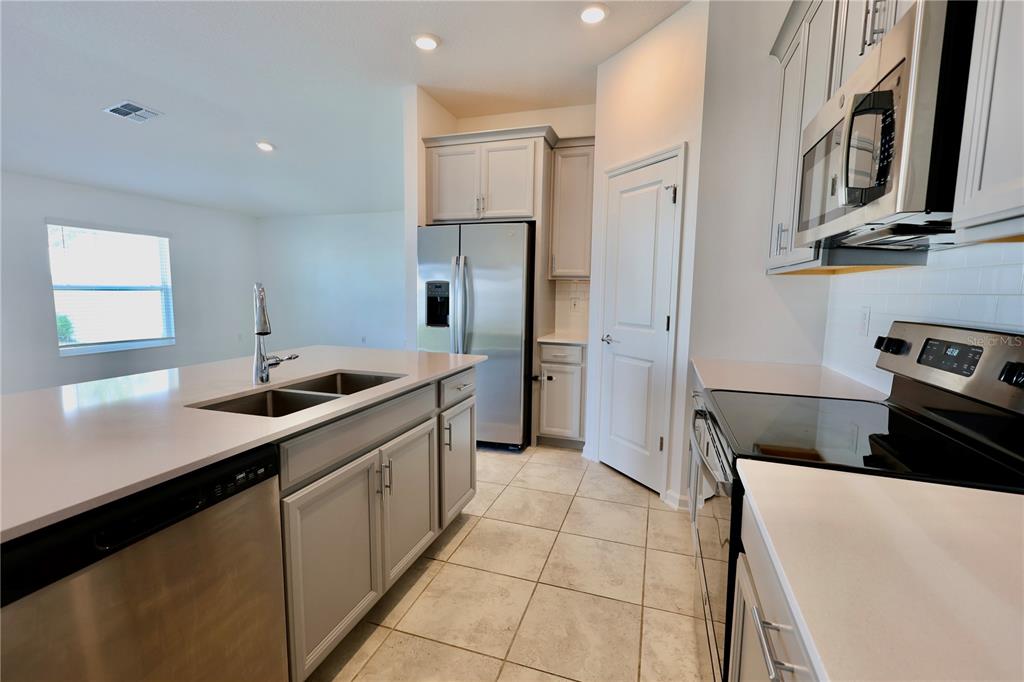 A kitchen features light gray cabinets, stainless steel appliances, a center island, and tile flooring — 965 LAUREL VIEW WAY, GROVELAND, FL
