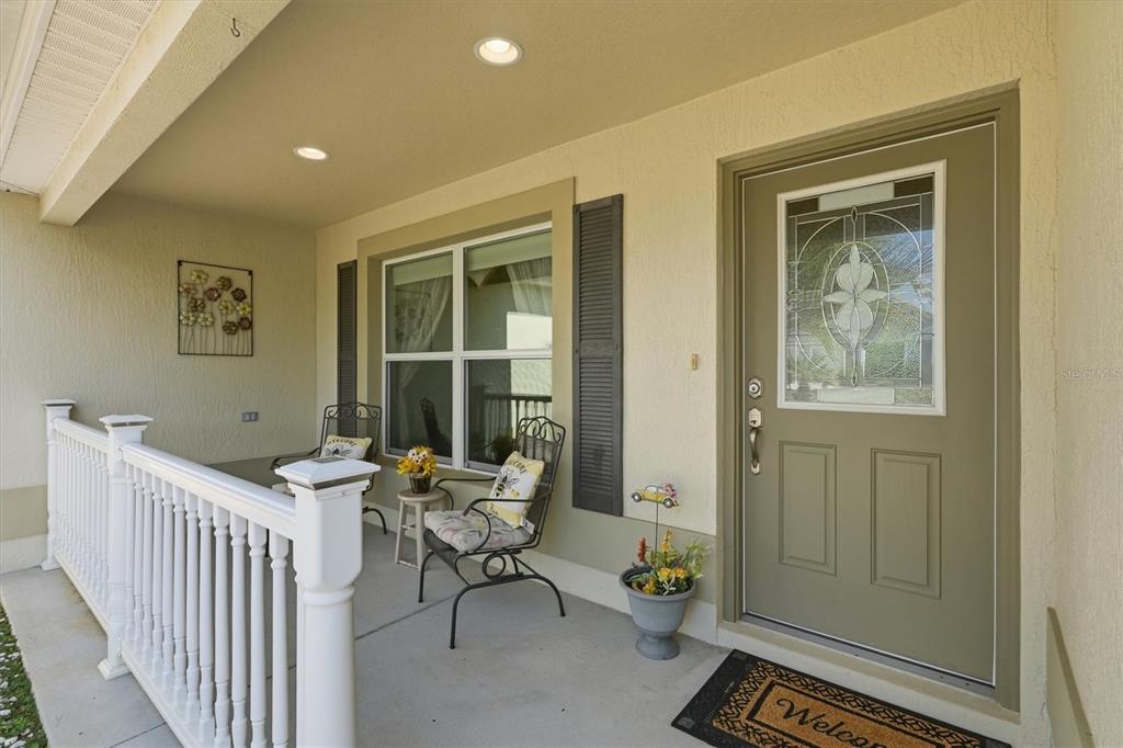 A covered front porch features a green door, white railing, and two metal chairs — 2007 YEARLING WAY, THE VILLAGES, FL