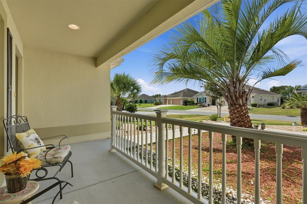 A covered porch features a metal chair, a small table with flowers, and a railing — 2007 YEARLING WAY, THE VILLAGES, FL