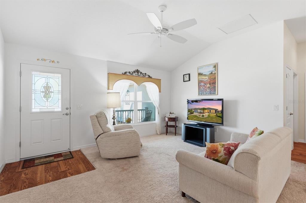 A living room features beige carpet, a white ceiling fan, a recliner, and a television — 2007 YEARLING WAY, THE VILLAGES, FL