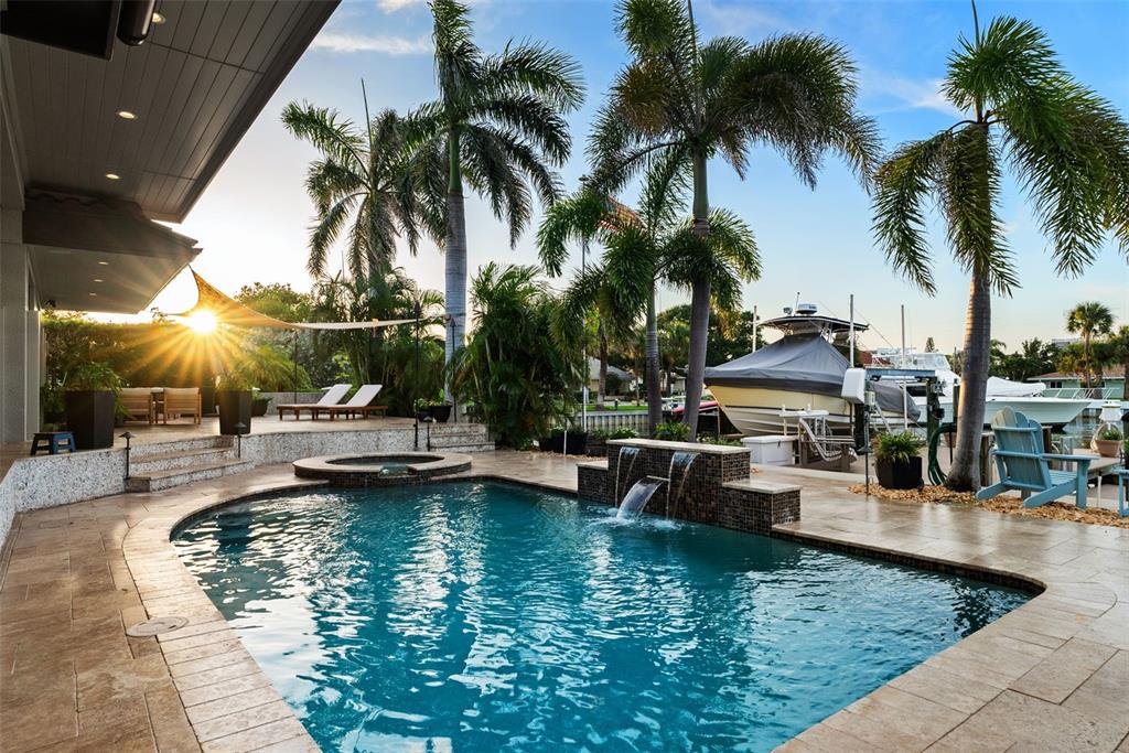 A swimming pool with a waterfall feature sits on a patio overlooking a boat dock — 203 HOWARD DRIVE, BELLEAIR BEACH, FL
