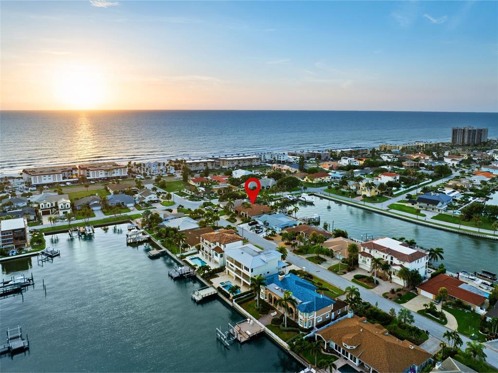 An aerial view shows waterfront homes along a canal near the ocean at sunset — 203 HOWARD DRIVE, BELLEAIR BEACH, FL