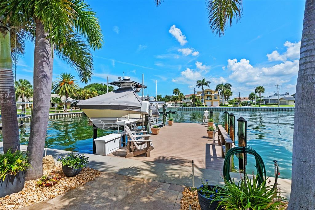 A boat on a lift sits at a wooden dock along a canal with palm trees — 203 HOWARD DRIVE, BELLEAIR BEACH, FL