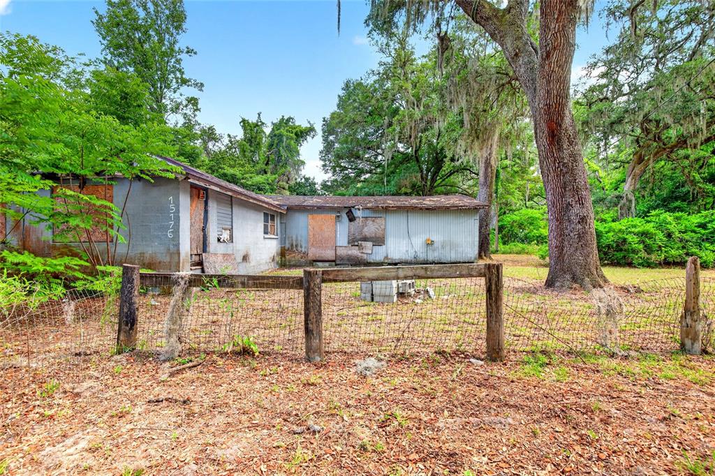 A weathered, single-story house with boarded-up windows sits behind a wire fence and trees — 15176 NE 154TH LANE, FORT MC COY, FL