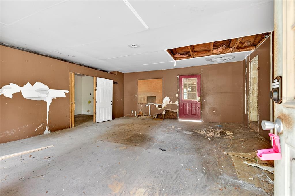 An unfinished room with brown walls, a damaged ceiling, and a red exterior door — 15176 NE 154TH LANE, FORT MC COY, FL