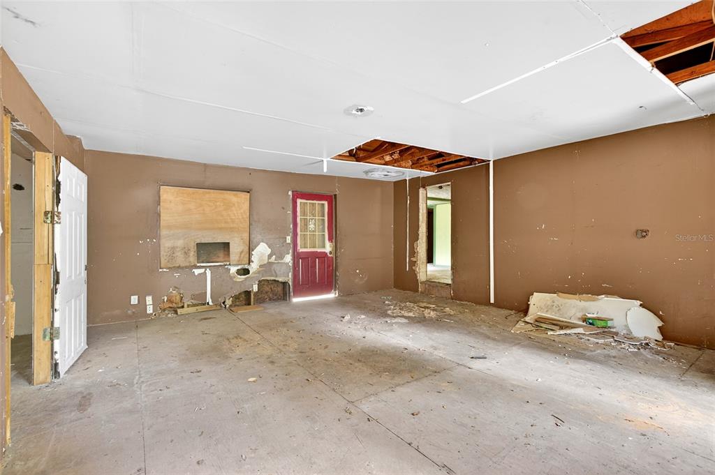 An unfinished room with brown walls, a red exterior door, and exposed ceiling joists — 15176 NE 154TH LANE, FORT MC COY, FL