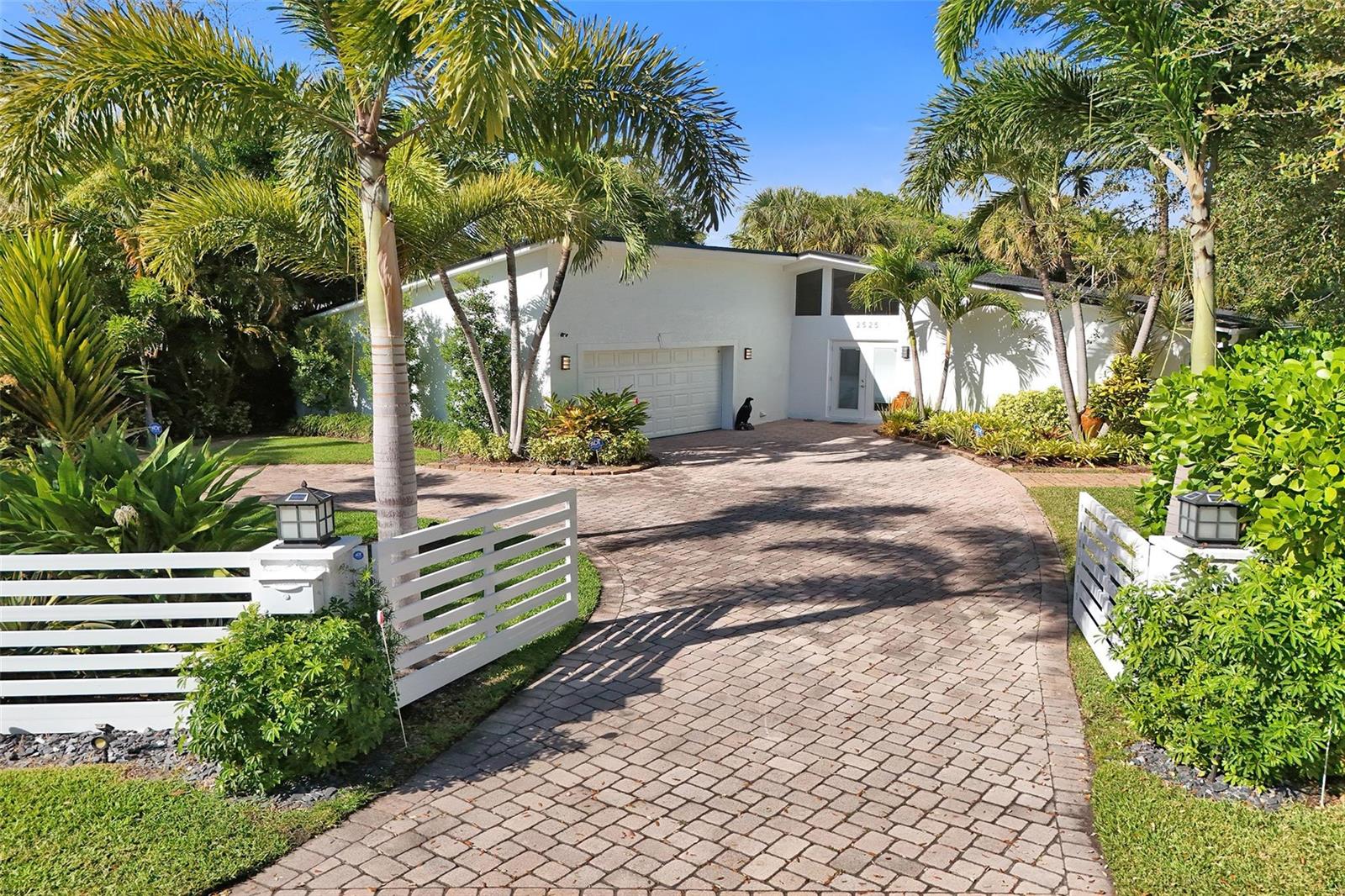 A white single-story house with a paved driveway and palm trees behind a white fence — 2525 SE 7th Drive, Pompano Beach FL 33062, POMPANO BEACH, FL