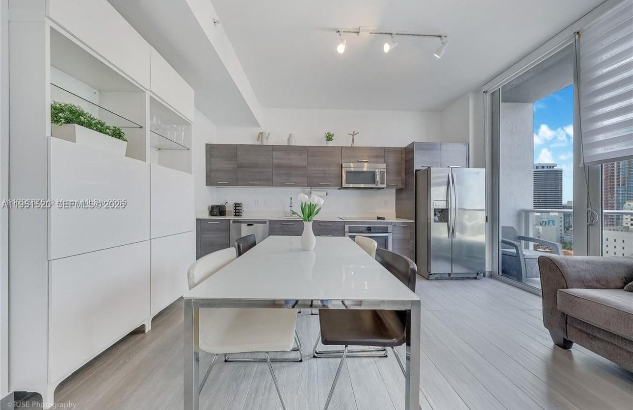 A modern kitchen and dining area features white cabinetry, gray wood-toned cabinets, and balcony access — 151 SE 1st St # 1706, Miami FL 33131, MIAMI, FL