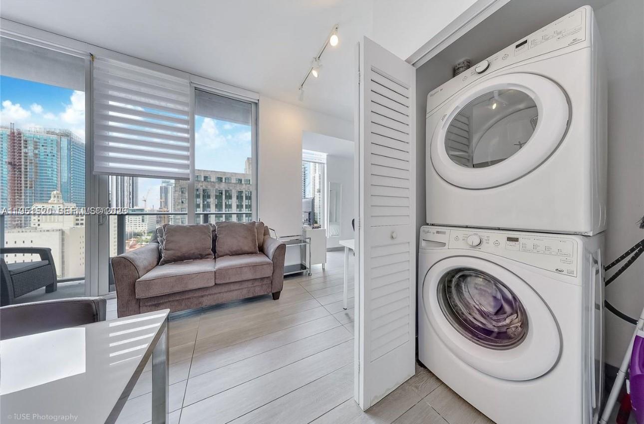 A room features a stacked washer and dryer, a gray sofa, and floor-to-ceiling windows — 151 SE 1st St # 1706, Miami FL 33131, MIAMI, FL
