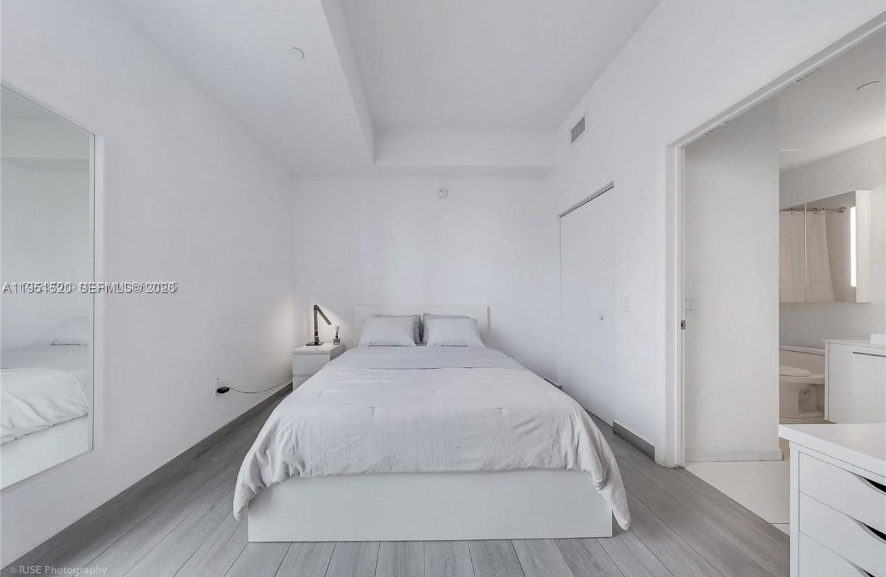 A minimalist bedroom features a bed, white walls, gray wood-look flooring, and an attached bathroom — 151 SE 1st St # 1706, Miami FL 33131, MIAMI, FL