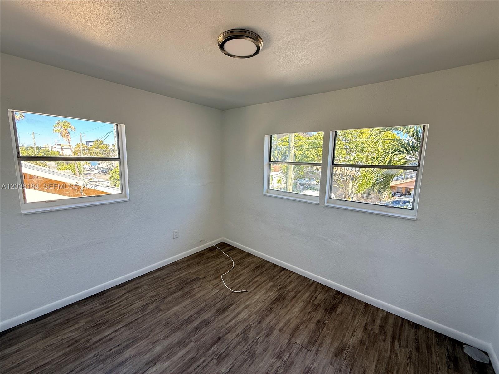 An empty bedroom features white walls, dark wood-look flooring, and three windows — 236 SW 10th Ave # B, Miami FL 33130, MIAMI, FL