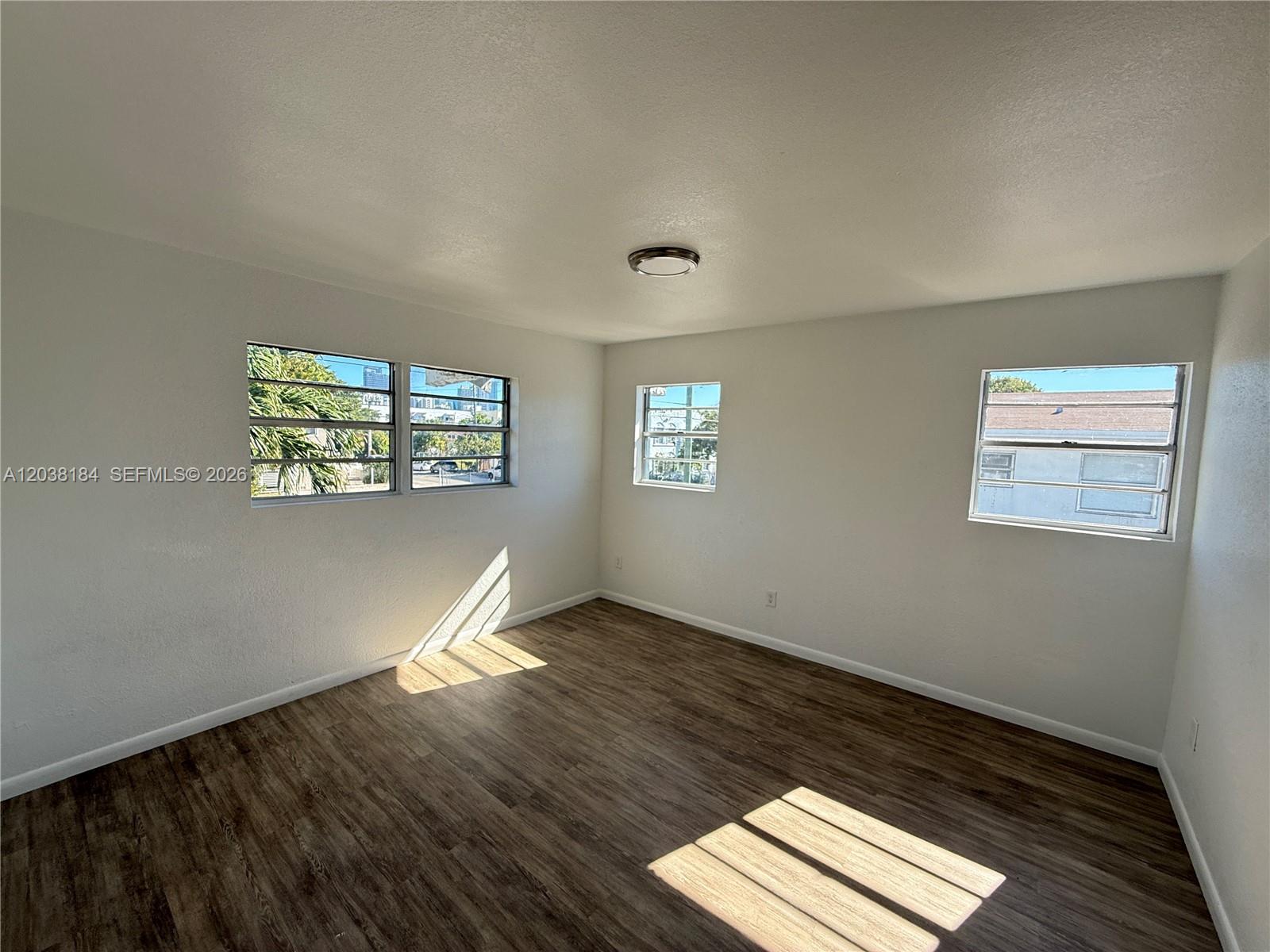 An empty room with white walls, wood-look flooring, and three windows — 236 SW 10th Ave # B, Miami FL 33130, MIAMI, FL