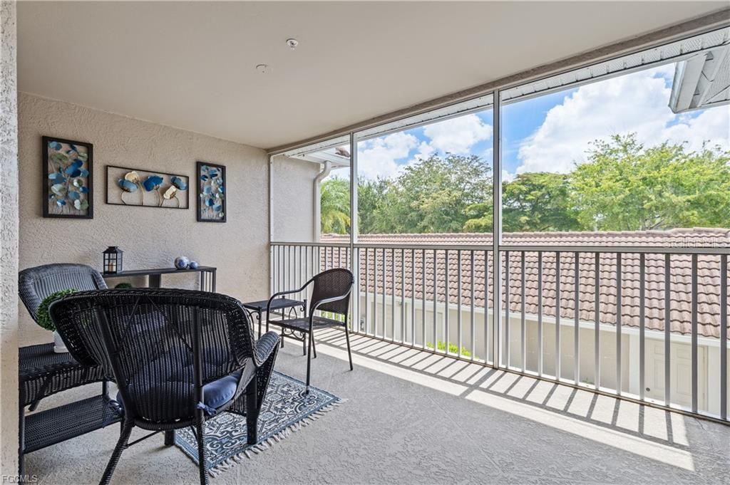 A screened-in balcony features wicker furniture, wall art, and views of surrounding trees and roofs — 10420 WINE PALM ROAD UNIT 5421, FORT MYERS, FL