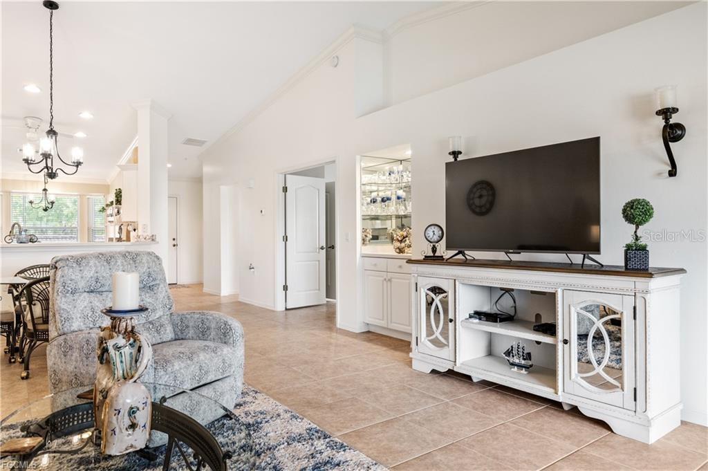 A living room features a patterned armchair, a media console with a television, and tile flooring — 10420 WINE PALM ROAD UNIT 5421, FORT MYERS, FL