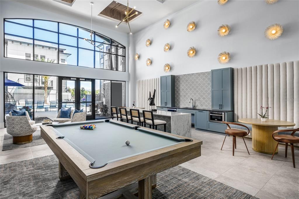 A modern lounge area features a pool table, kitchenette, and large windows overlooking a pool — 20191 SABAL PALM COURT UNIT B2, LAND O LAKES, FL