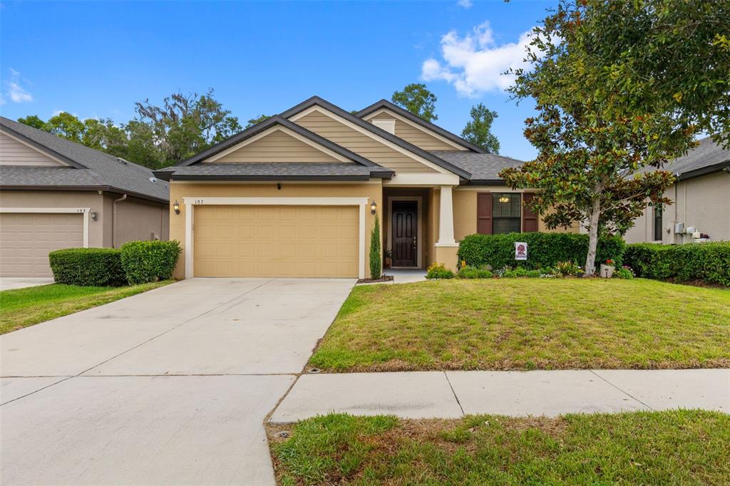 A single-story suburban house with a tan stucco exterior, a two-car garage, and a lawn — 107 ELINA SKY DRIVE, SEFFNER, FL