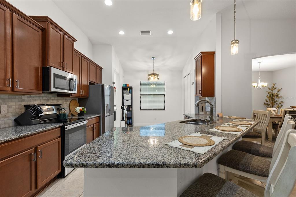 A kitchen with wood cabinets, granite countertops, a large island, and stainless steel appliances — 107 ELINA SKY DRIVE, SEFFNER, FL