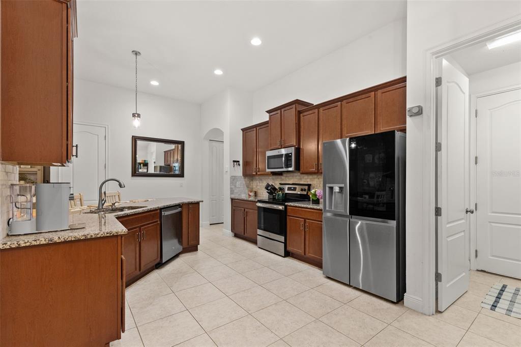A kitchen features wood cabinets, granite countertops, stainless steel appliances, and light tile flooring — 107 ELINA SKY DRIVE, SEFFNER, FL