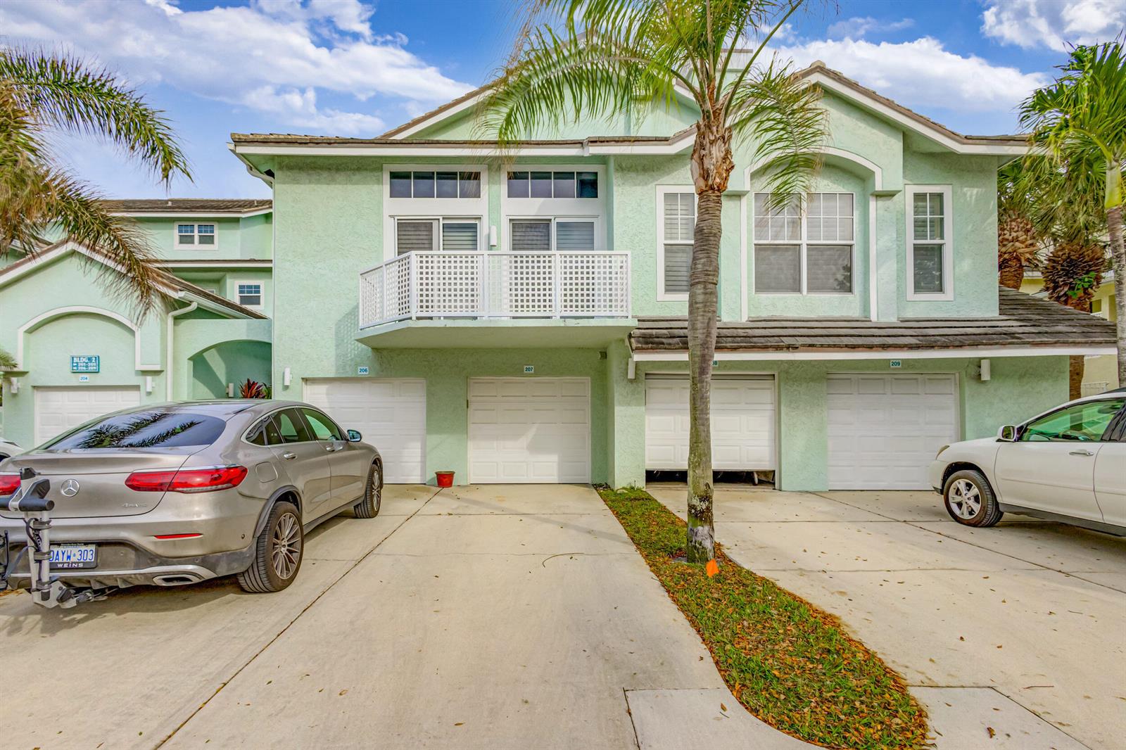 A light green multi-unit residential building with four garage doors and a palm tree — 207 Mainsail Circle, Jupiter FL 33477, JUPITER, FL