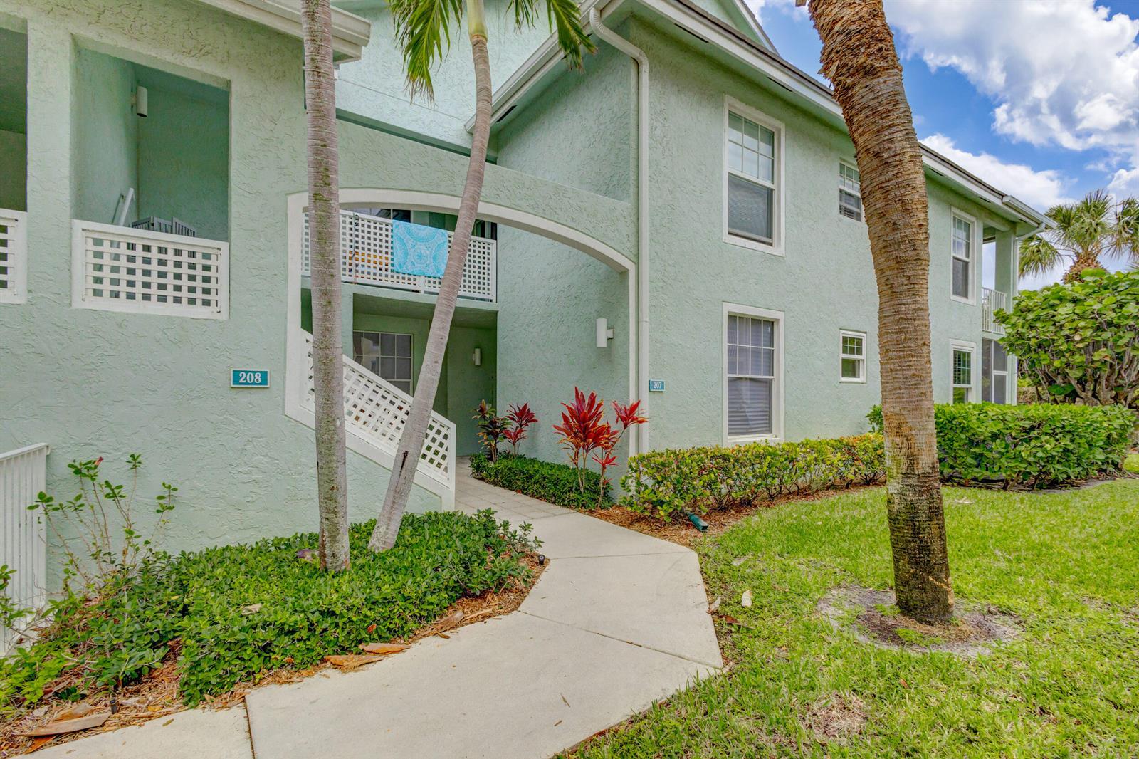 A light green two-story building features a concrete walkway leading to unit 208 — 207 Mainsail Circle, Jupiter FL 33477, JUPITER, FL
