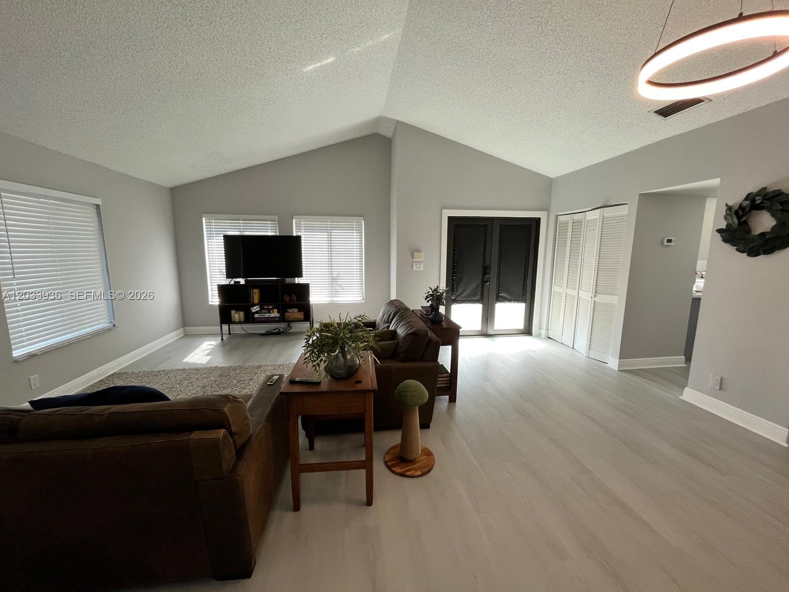 A living room features vaulted ceilings, light wood-look flooring, and a brown leather sofa — 3931 SW 84th Ter, Davie FL 33328, DAVIE, FL