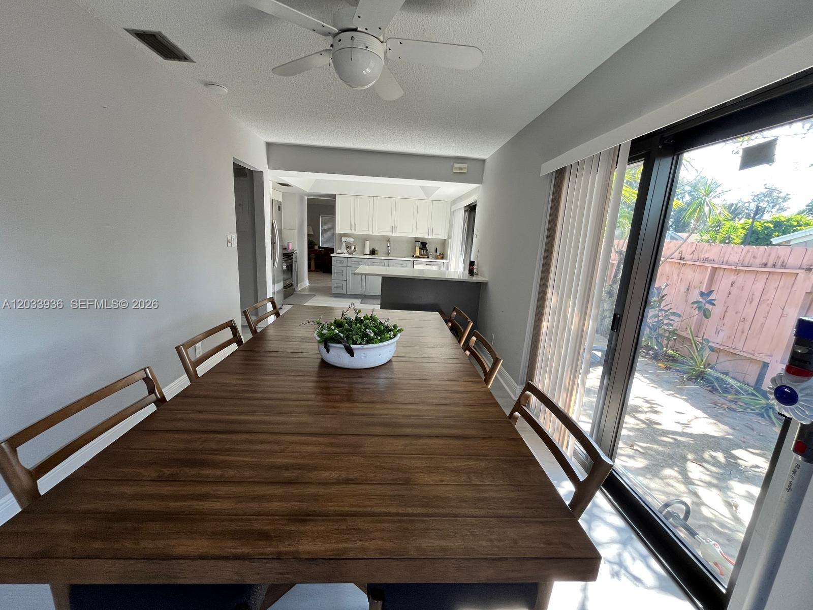 A dining area with a wooden table leads to a kitchen and a sliding glass door — 3931 SW 84th Ter, Davie FL 33328, DAVIE, FL