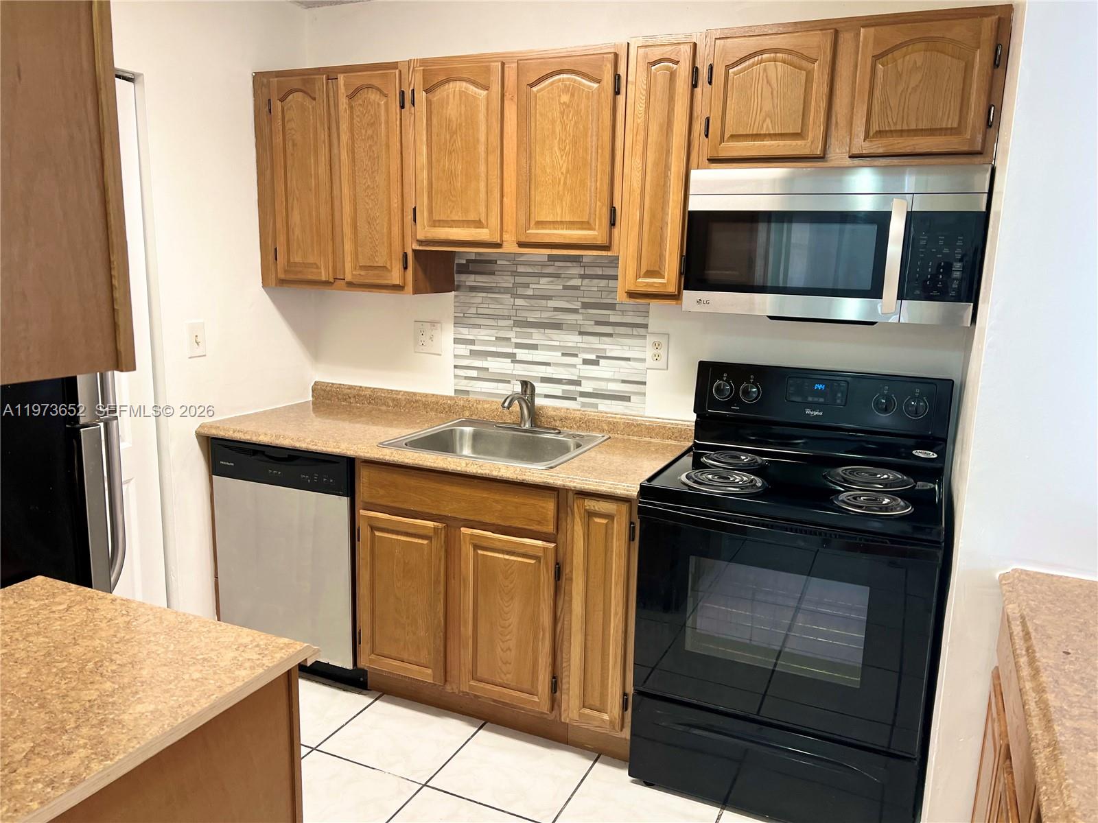 A kitchen features wood cabinets, a stainless steel dishwasher, a black stove, and tile flooring — 20761 NE 4th Pl # 104, Miami FL 33179, MIAMI, FL