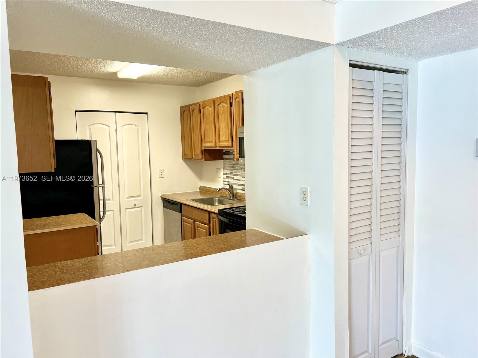 A kitchen with wood cabinets and a pass-through counter overlooks a white-walled living area — 20761 NE 4th Pl # 104, Miami FL 33179, MIAMI, FL
