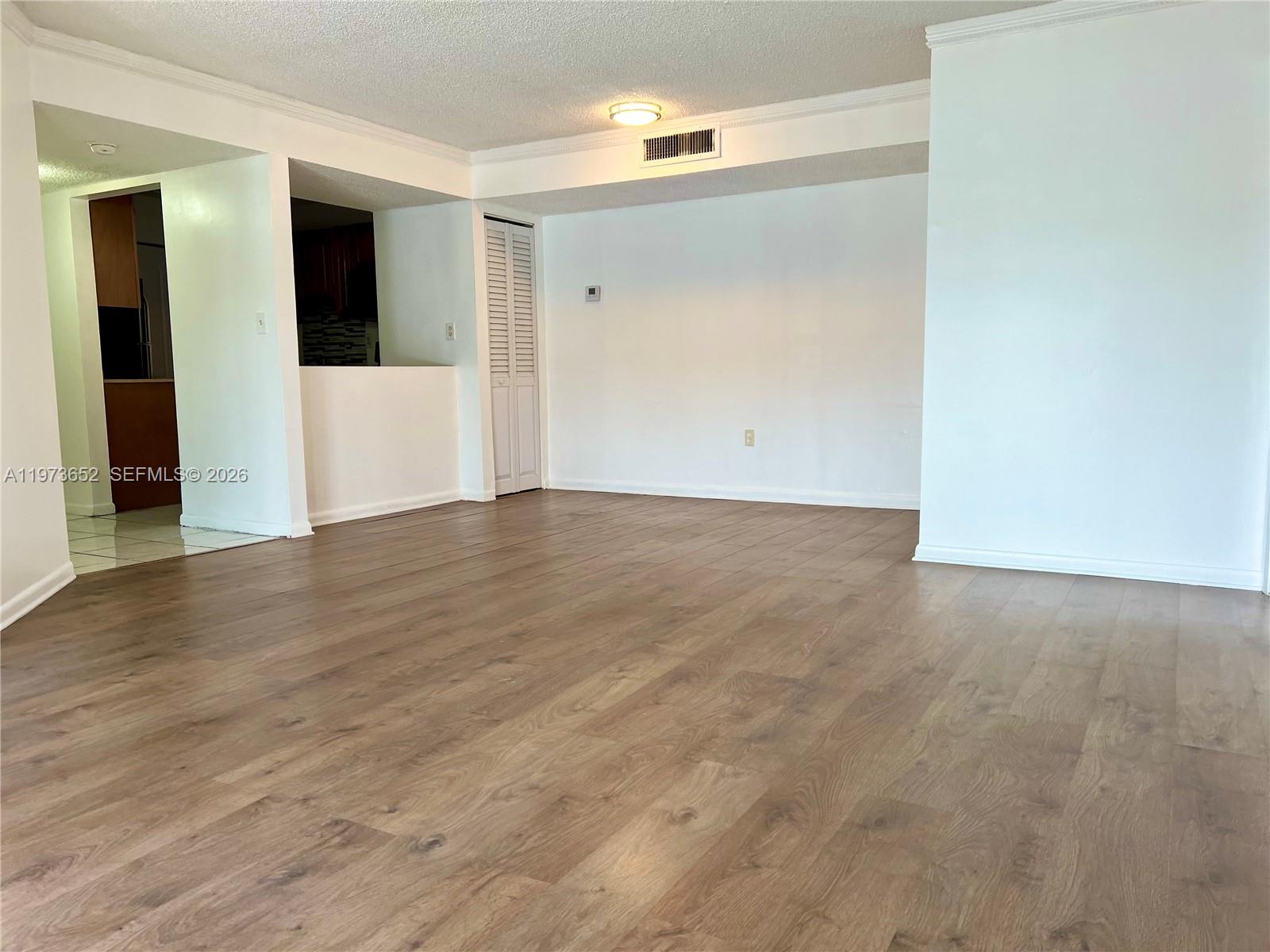 An empty living room features wood-look laminate flooring, white walls, and a recessed ceiling light — 20761 NE 4th Pl # 104, Miami FL 33179, MIAMI, FL