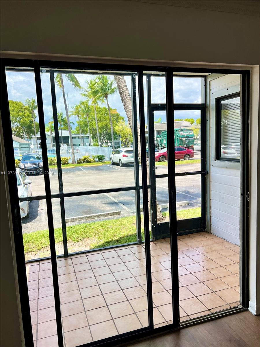 A tiled screened-in porch looks out onto a parking lot and palm trees — 20761 NE 4th Pl # 104, Miami FL 33179, MIAMI, FL
